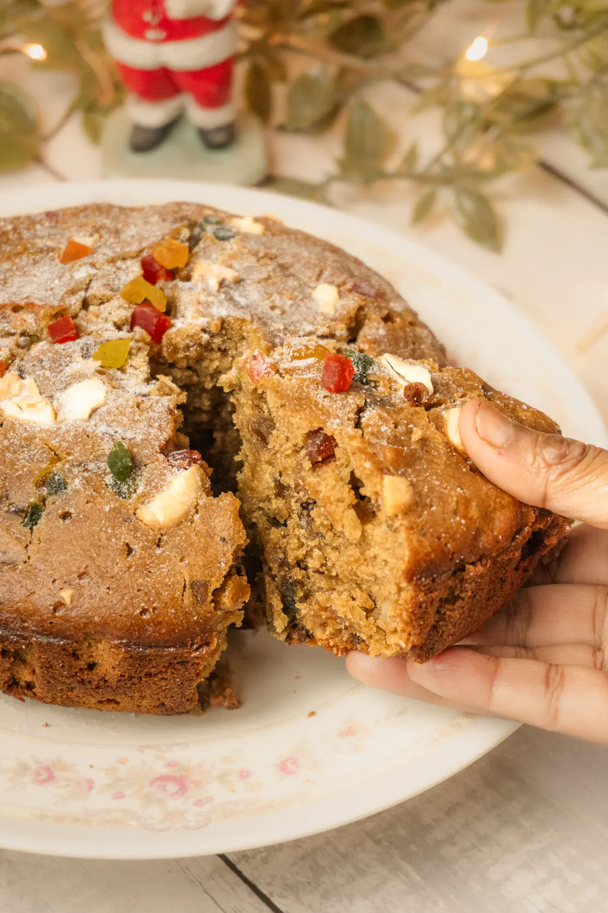 A hand pulling apart a slice of dark fruit cake studded with cherries