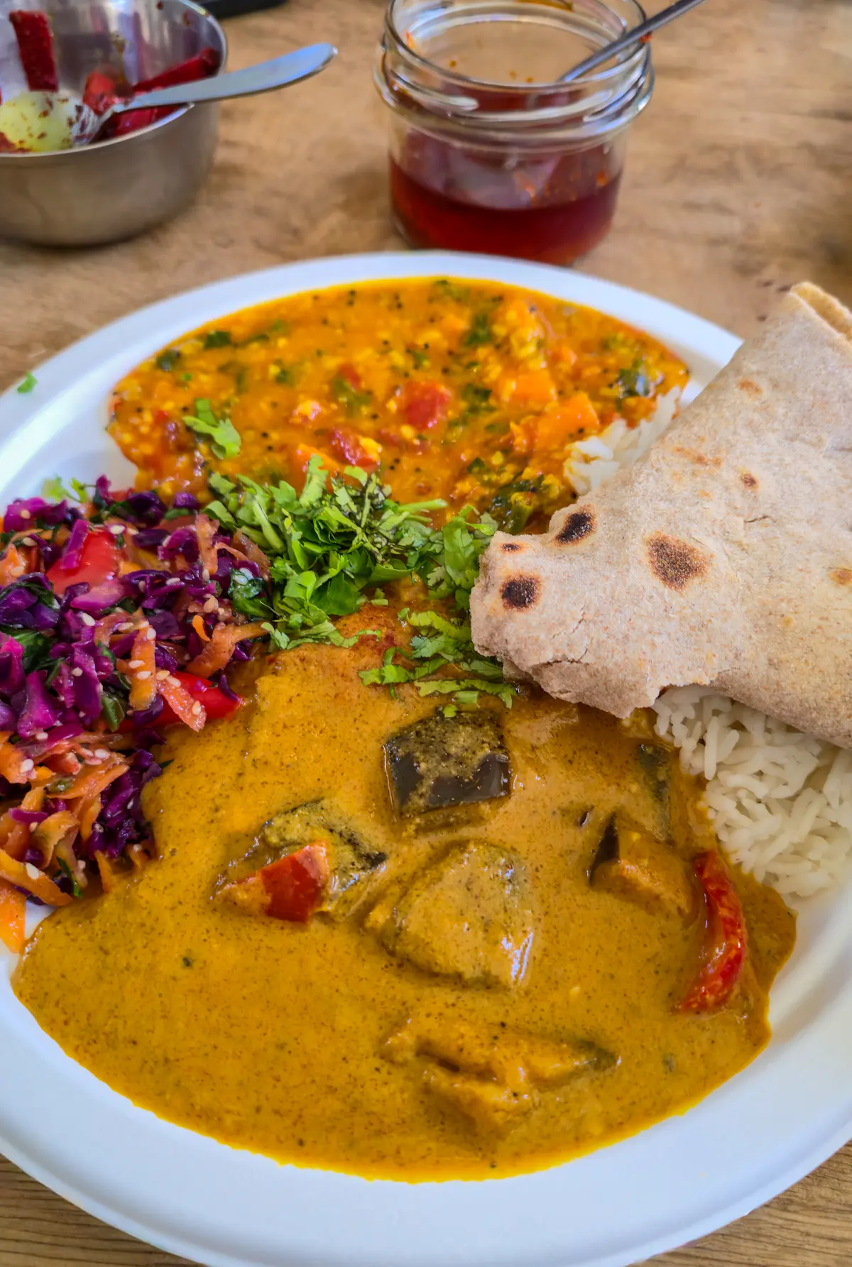 A plate of chicken curry with a soft roti folded on the side, slaw and rice